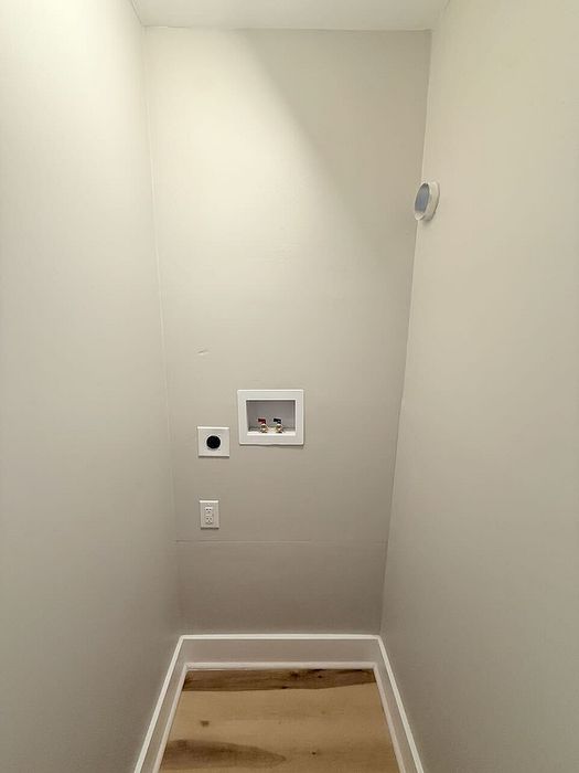 Compact laundry space with modern hookups and sleek wooden flooring, ideal for efficient urban living.