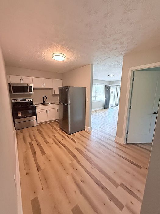 Bright kitchen area with modern stainless steel appliances, sleek white cabinetry, and elegant wood flooring leading into an airy living space.