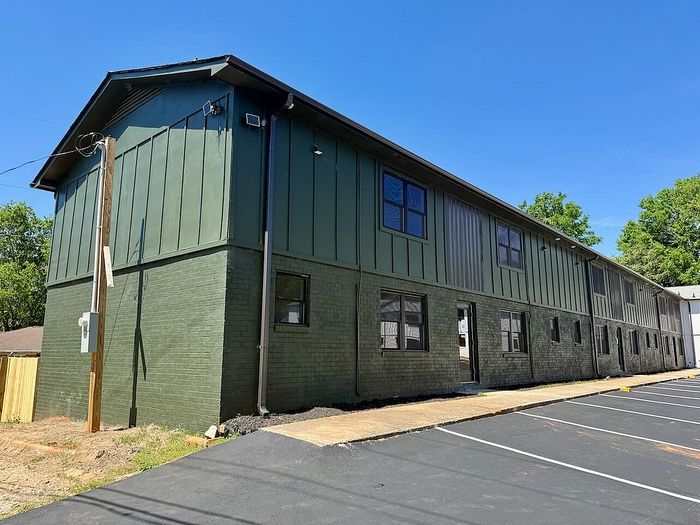 Modern two-story apartment complex with sleek green exterior and ample parking, set against a clear blue sky.