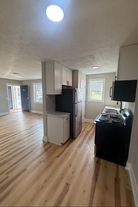 Bright, open kitchen with stainless steel appliances and modern wood flooring leading to a spacious living area.