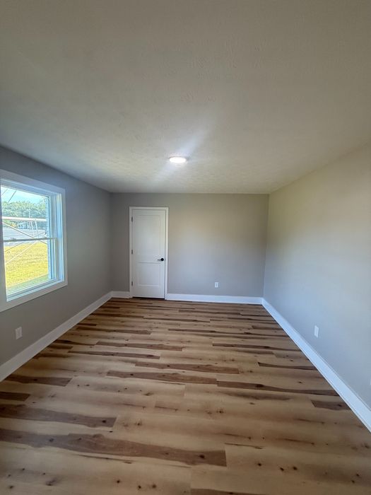 Bright, unfurnished room with elegant wood flooring, large window, and gray walls, ideal for customization.