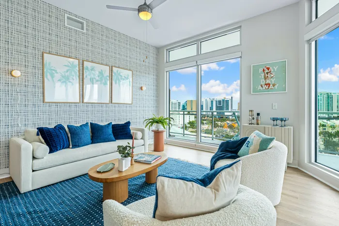 A modern living room at The DeSOTA featuring a blue and white color scheme, with large windows overlooking the city skyline.