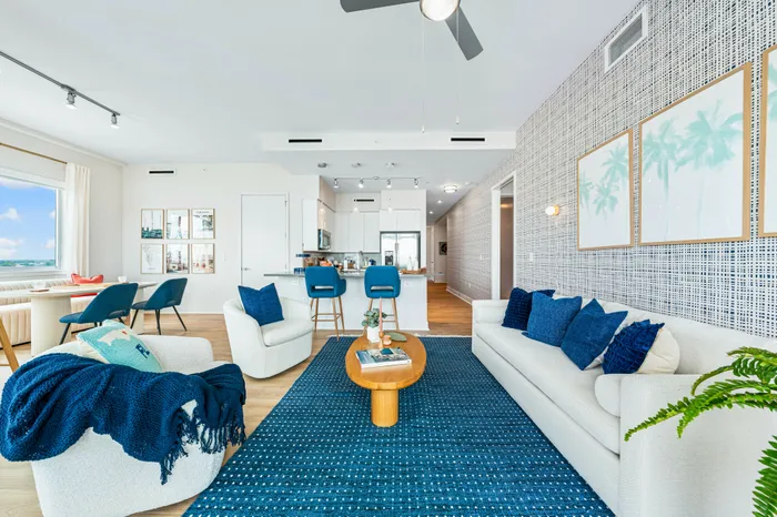 An open-concept living, dining, and kitchen area at The DeSOTA, with a modern blue and white color scheme and a patterned accent wall.