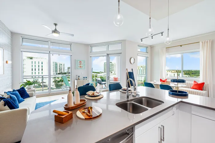A bright, open-concept apartment in Sarasota, FL, with a large kitchen island, a dining area, and a balcony with a stunning city and water view.