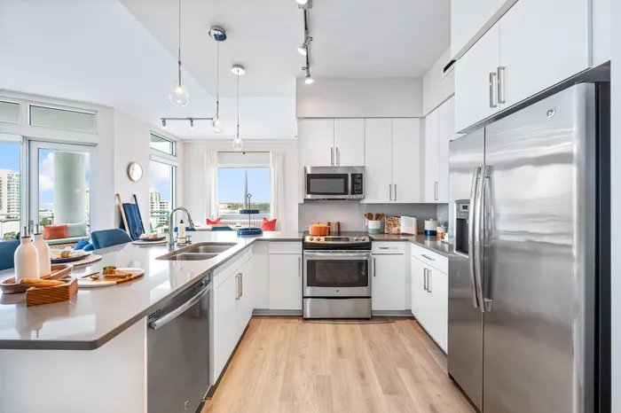 A modern kitchen in a Sarasota, FL apartment, with white cabinets, stainless steel appliances, a large island, and an open living area.