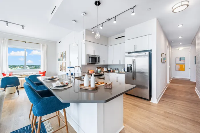 An open-concept kitchen and living area at The DeSOTA with a large island and blue bar stools, modern appliances, and a dining nook.