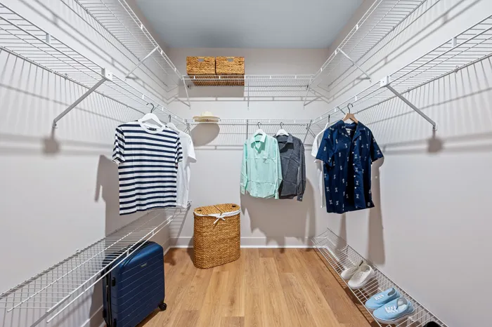A spacious walk-in closet in a The DeSOTA apartment, featuring white wire shelving, hanging clothes, and a laundry basket on a wood floor.
