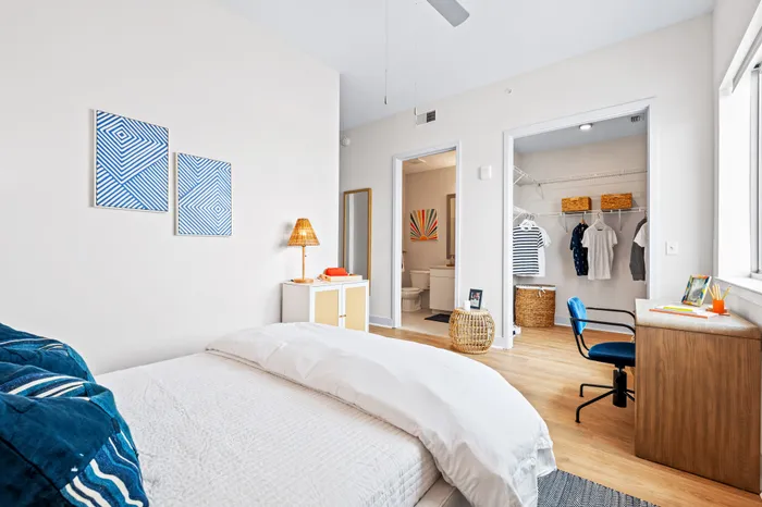 A modern bedroom at The DeSOTA with a bed, a desk area, and an open doorway leading to a walk-in closet and a full bathroom.