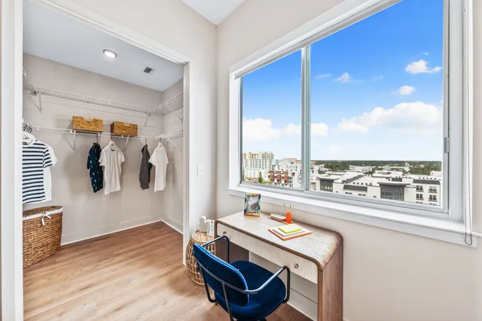 A walk-in closet and study nook in a Sarasota, FL apartment, with a desk, blue chair, and a large window overlooking the city.