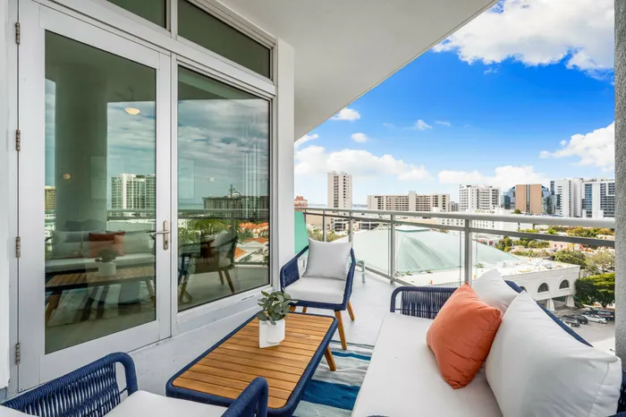 A spacious balcony at The DeSOTA with modern outdoor seating, a striped rug, and a scenic view of the city and blue sky.