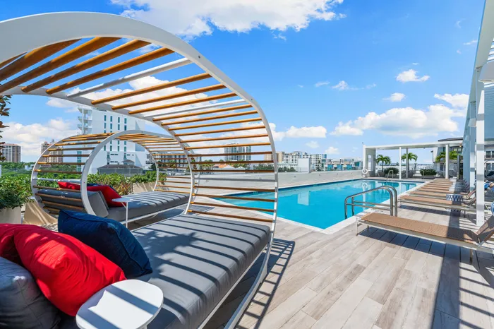A rooftop pool deck in Sarasota, FL, with unique, curved daybeds, lounge chairs, and a pool, overlooking the city skyline.