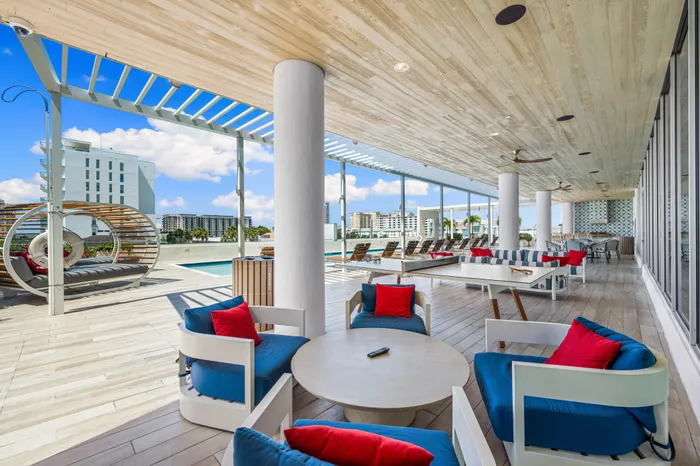 A resort-style outdoor lounge at The DeSOTA with multiple seating areas, a modern pergola, a pool deck, and a view of the city.