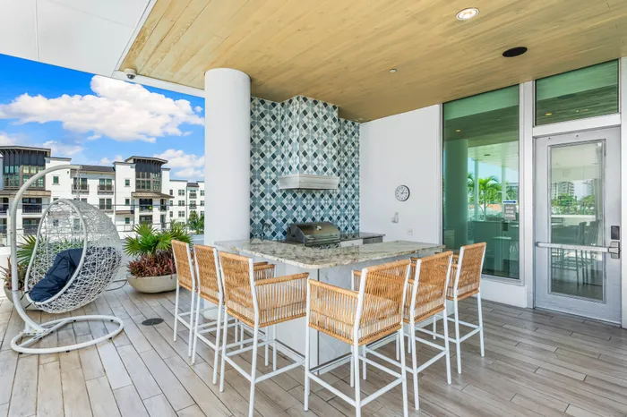 An outdoor grilling station at The DeSOTA, with a tiled backsplash, bar seating, and a unique hanging egg chair on a wood deck.