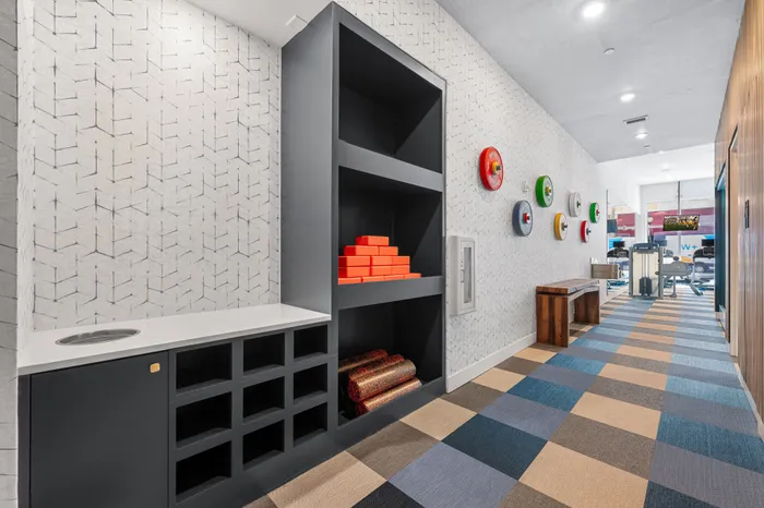 A modern fitness studio at The DeSOTA with a gray storage unit, a colorful checkered floor, and patterned wallpaper on the wall.