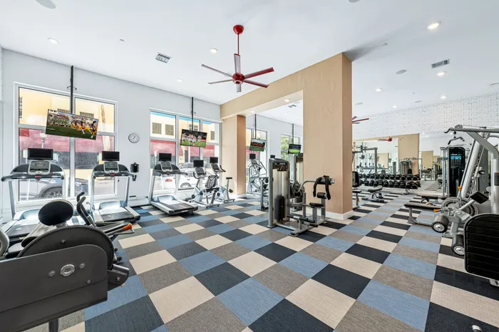 A well-equipped fitness center at The DeSOTA with multiple cardio machines, free weights, and a colorful checkered floor.