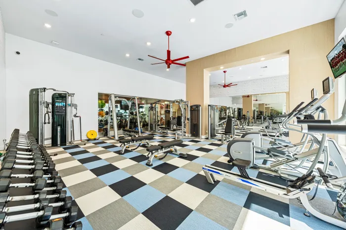 A modern fitness center at The DeSOTA with a variety of weight machines, benches, and free weights, all on a colorful checkered floor.