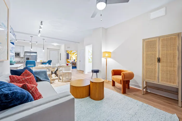 A spacious living area in an apartment at The DeSOTA with modern furniture in blue and orange, an open kitchen, and a dining area.