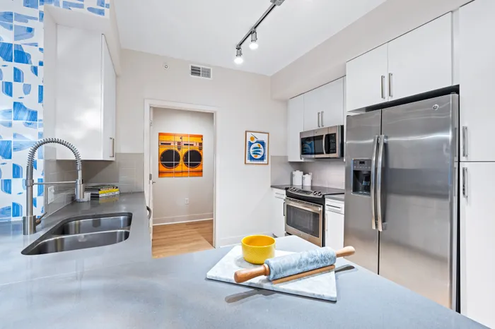 A modern kitchen in The DeSOTA with a gray island, stainless steel appliances, white cabinets, and a bold blue and white patterned wall.