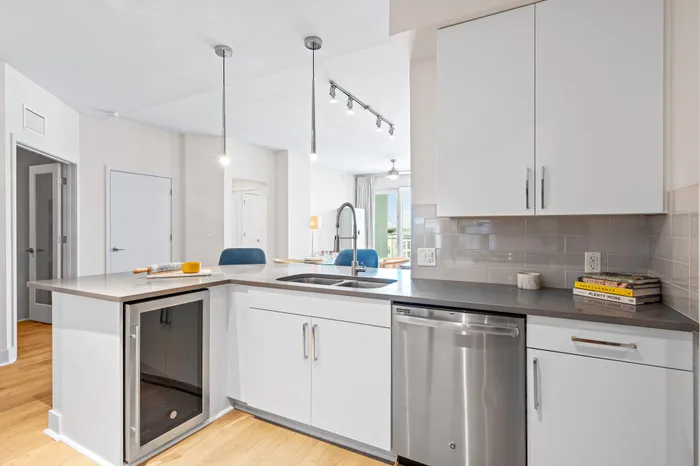 A modern kitchen at The DeSOTA with a spacious island, a wine cooler, stainless steel appliances, and sleek white cabinets.