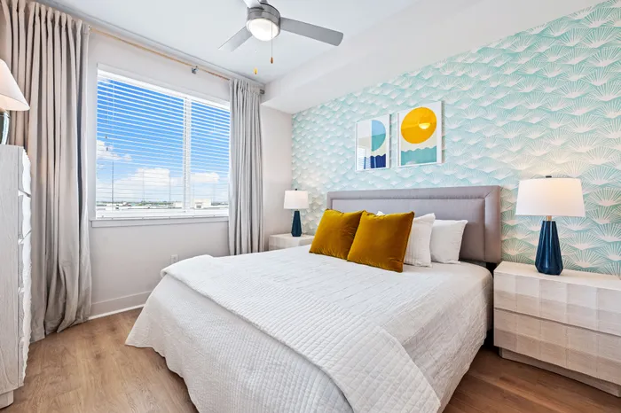 A modern bedroom in a Sarasota, FL apartment with patterned wallpaper, a gray bed, and bright yellow accent pillows.