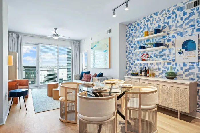 An open-concept living and dining area at The DeSOTA with a glass table, modern chairs, and a bold blue and white patterned accent wall.