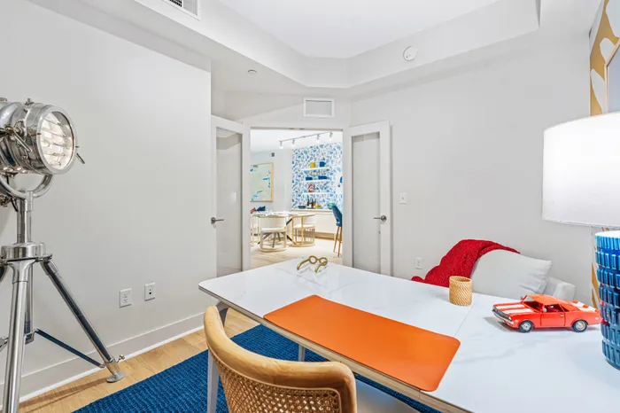 A modern home office in a The DeSOTA apartment with a desk, a vintage-style light, and a view into a colorful dining room.