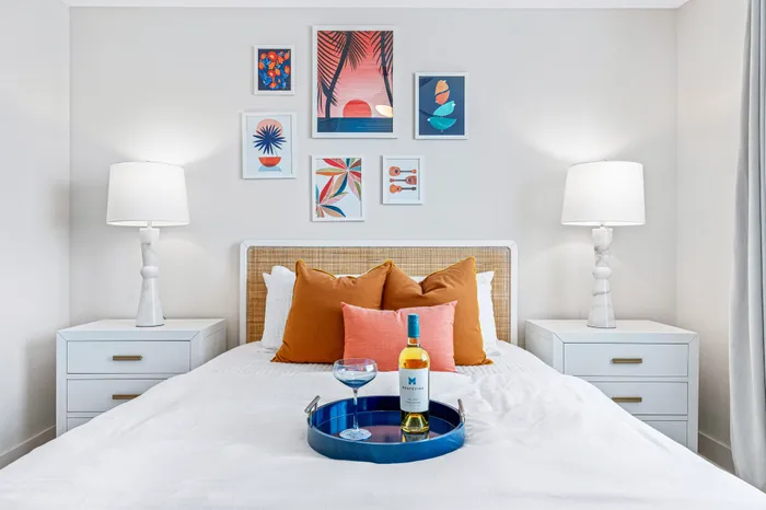 A modern bedroom at The DeSOTA with a bed, two nightstands, and a gallery of framed tropical art on the wall above the headboard.