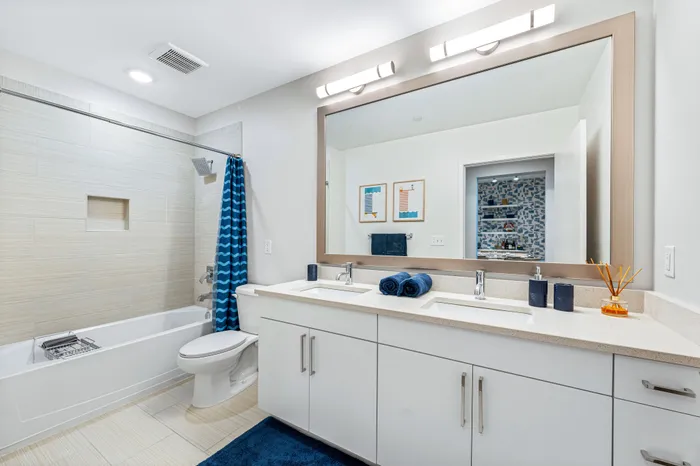 A modern bathroom at The DeSOTA with a double vanity, a large mirror, a toilet, and a bathtub with a blue patterned curtain.