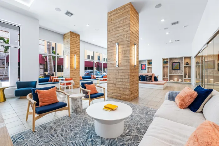A modern apartment lobby at The DeSOTA with stylish blue and orange seating, wood-paneled columns, and a large patterned rug.