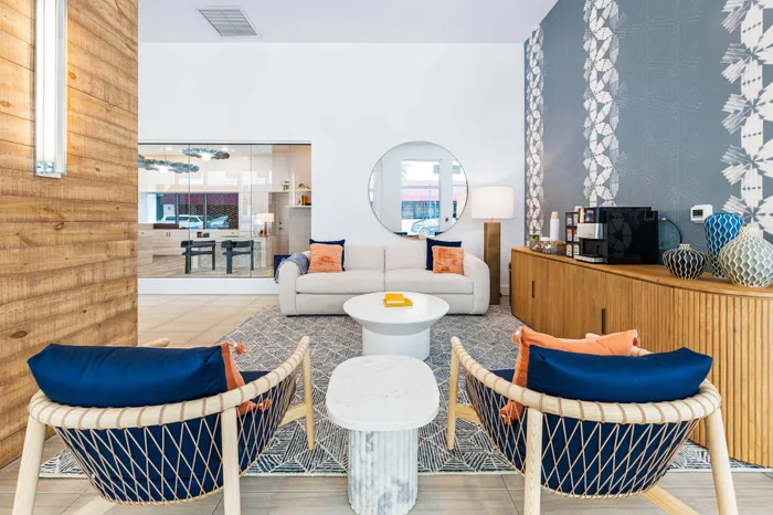 A modern lounge at The DeSOTA with blue and orange seating, a white sofa, and a coffee bar, set against a patterned accent wall.