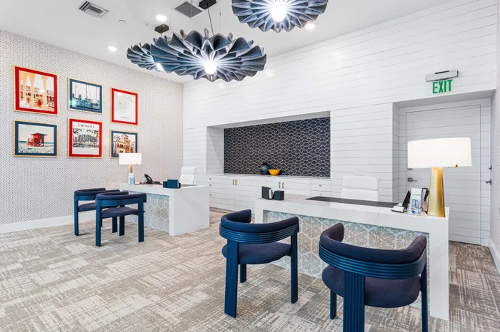 A modern leasing office at The DeSOTA with unique blue chairs, patterned wallpaper, and distinctive light fixtures over the desks.