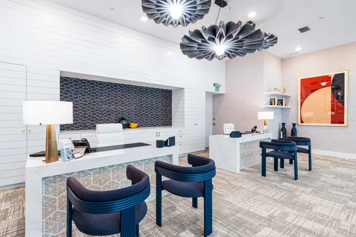 A modern leasing office at The DeSOTA with unique chairs, patterned walls, and two desks with distinctive geometric bases.