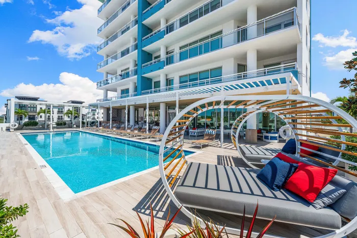 A resort-style pool deck at The DeSOTA with a unique curved daybed, modern lounge chairs, and a swimming pool next to the building.