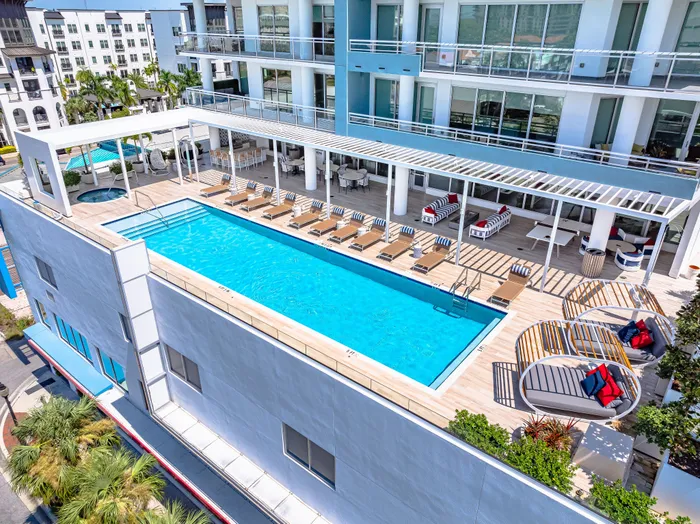 A rooftop pool and lounge area in Sarasota, FL, with rows of chaise lounges, daybeds, and a hot tub under a modern pergola.