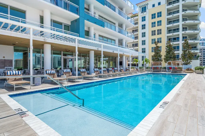 A resort-style swimming pool at The DeSOTA with lounge chairs under a pergola, adjacent to the modern building with balconies.