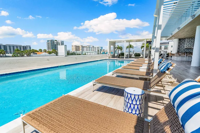 A rooftop swimming pool at downtown Sarasota, FL, with lounge chairs on a wood deck, overlooking the scenic city skyline.