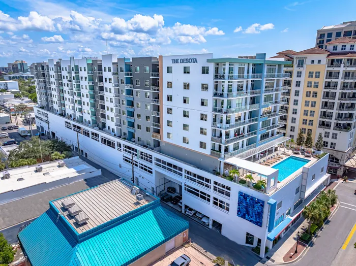An aerial view of The DeSOTA apartment building in downtown Sarasota, featuring a modern facade, balconies, and a rooftop pool.