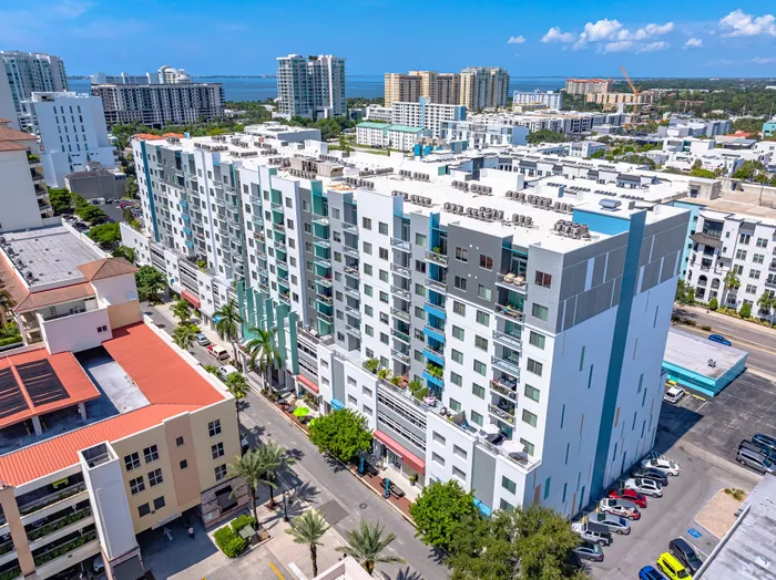 An aerial view of a modern multi-story apartment building in downtown Sarasota, featuring balconies and a white, gray, and blue facade.