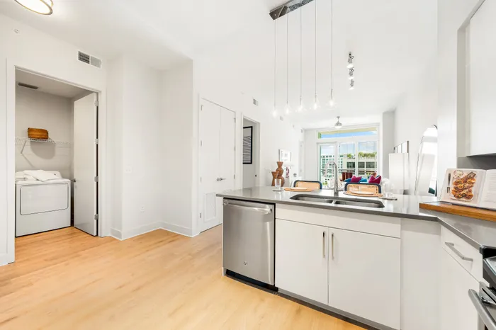 An open-concept kitchen in a The DeSOTA apartment with an island and a view of the laundry closet and the living room.