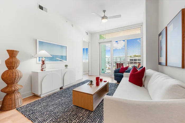 A modern living room in a The DeSOTA apartment with a white sofa, a large patterned rug, and a balcony with a city view.