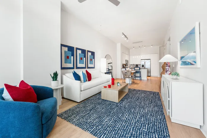 An open-concept living room in a The DeSOTA apartment, with a blue and red color scheme, a patterned rug, and a view into the kitchen.