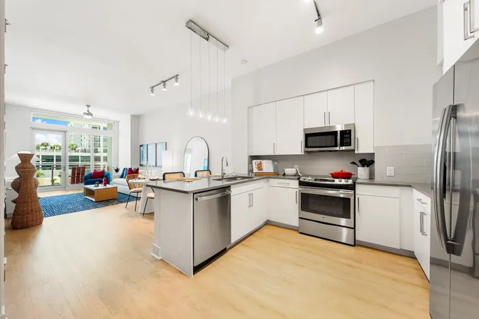 An open-concept living room and kitchen in a The DeSOTA apartment with modern appliances, a large island, and a balcony with a city view.