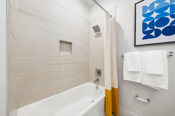 A modern bathroom in a The DeSOTA apartment with a bathtub, textured tile walls, a unique shower curtain, and wall art.