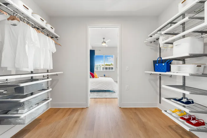 A spacious walk-in closet in a The DeSOTA apartment with shelving for clothes and baskets, with a view of the bedroom.