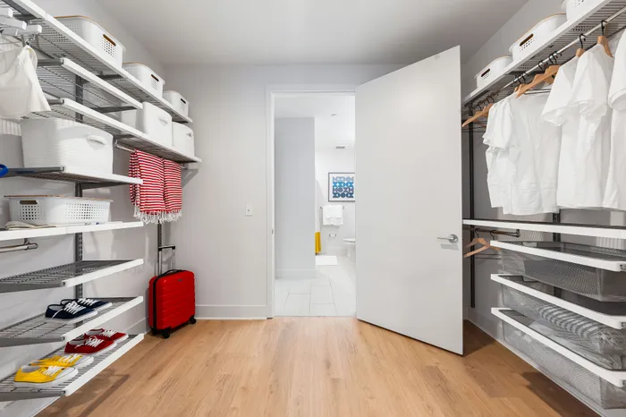 A spacious walk-in closet in a The DeSOTA apartment with shelving for clothes and shoes, and an open doorway leading into a bathroom.