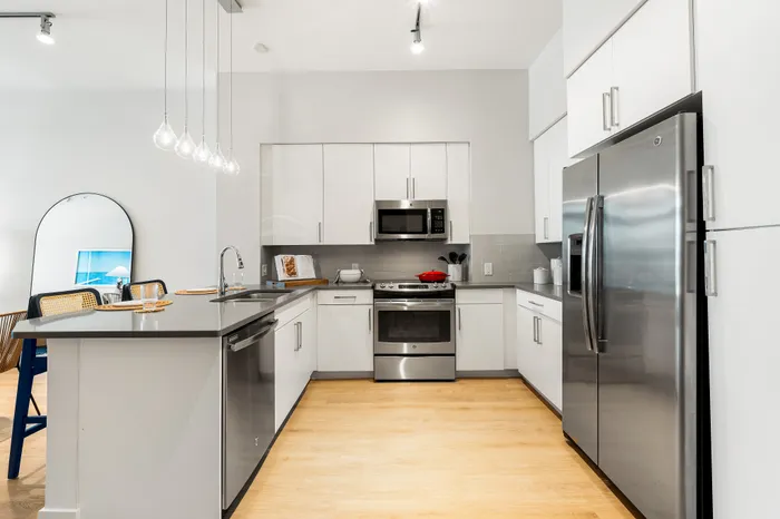 A modern U-shaped kitchen in a The DeSOTA apartment with white cabinets, stainless steel appliances, and a central island.