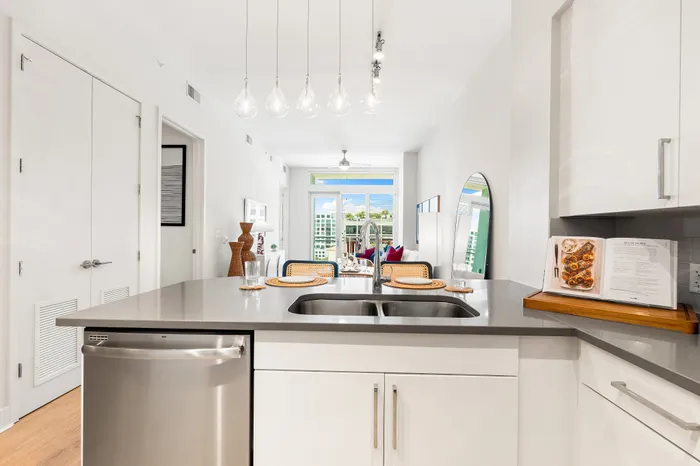 A modern kitchen island in a The DeSOTA apartment with a double sink and a view into the open-concept living area with a balcony.