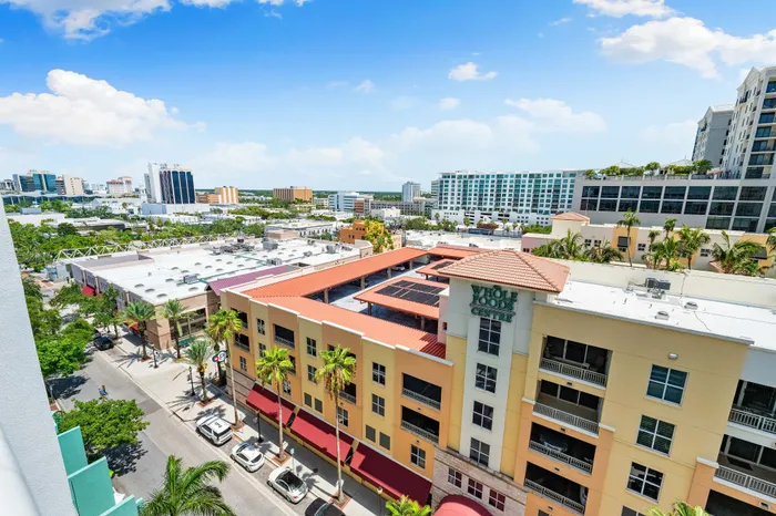 An aerial view of a busy street in Sarasota, FL, with a Whole Foods building in the foreground and a dense urban skyline.