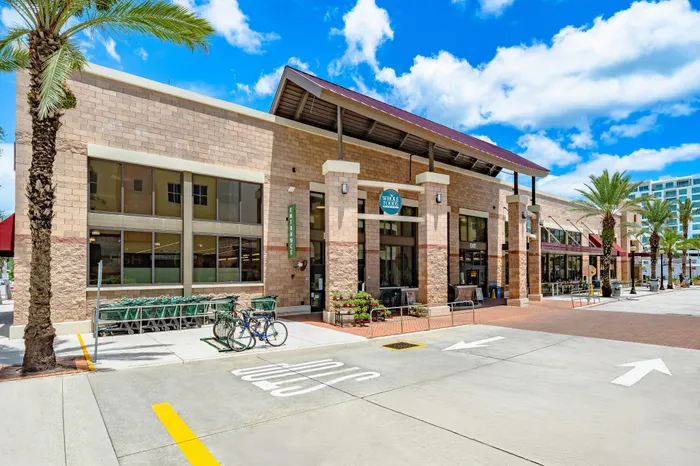 The exterior of a modern Whole Foods market in Sarasota, FL, with a brick facade, shopping carts, and palm trees in front.
