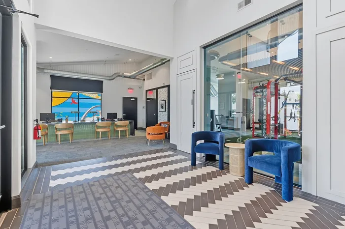 Modern and inviting community area with stylish seating, vibrant mural, and state-of-the-art fitness center view.
